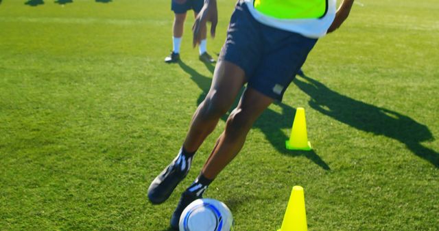 This depicts a soccer player practicing dribbling on a grass field with training cones. Useful for sports training materials, soccer coaching guides, athletic programs, and youth sports promotions.
