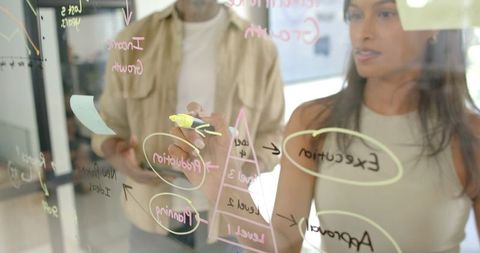 Diverse Colleagues Brainstorm on Glass Board in Modern Office