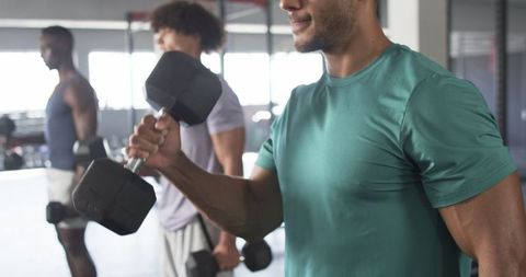 Diverse men exercising in modern gym using dumbbells