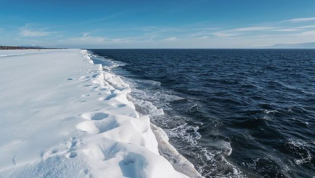 Snow-covered shoreline meeting dark choppy ocean with wind-sculpted ice drifts