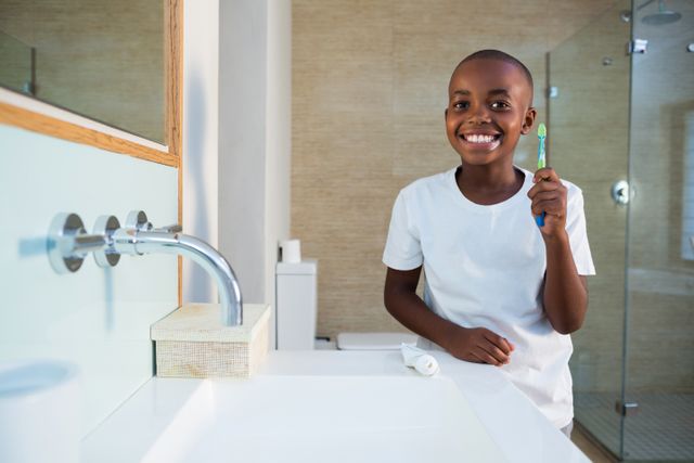 Portrait of smiling boy showing toothbrush while standing by sink at bathroom