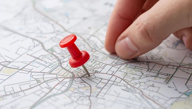Red pushpin marking city road map intersection with fingertips for navigation planning