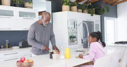 African american father slicing bread while daughter stirring at bright kitchen island