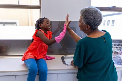 Grandmother granddaughter sharing high-five over kitchen sink during chores and bonding