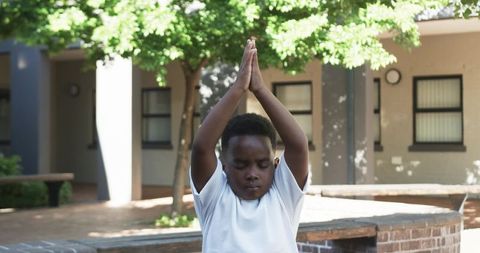 Child practicing mindful yoga in courtyard pressing palms together with closed eyes
