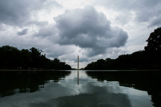 Dramatic cloudy sky over Washington Monument reflecting in the pool, creating a serene yet intense atmosphere. Perfect for themes involving history, nature, and outdoor activities. Ideal for travel brochures, educational materials, and mood-setting background images for websites.
