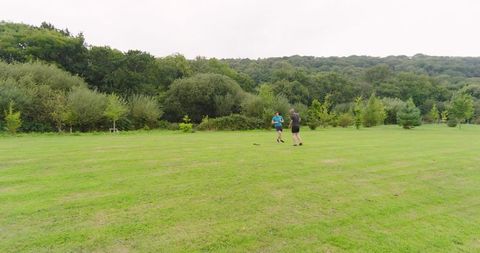 Two Men Jogging on Grass Amidst Green Woodland Scenery