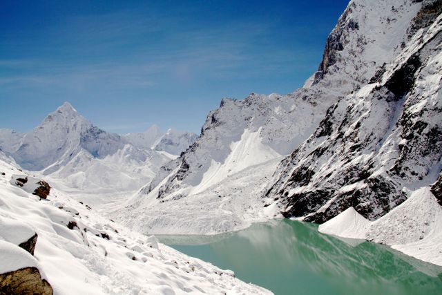 Majestic snow-covered Himalayan mountains surrounding a turquoise glacial lake under a clear blue sky. Perfect for travelers, nature lovers, and editors looking for spectacular mountain scenery in winter. Ideal for use in travel brochures, outdoor adventure promotions, environmental campaigns, and mindfulness content.