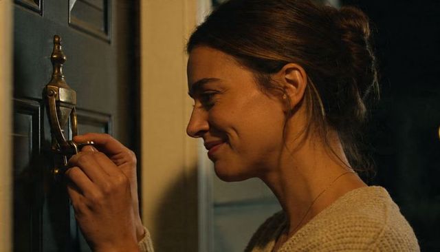 Woman unlocking brass door knocker and turning key at front door at night