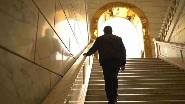 Man climbing marble staircase toward glowing archway light, silhouette and reflection