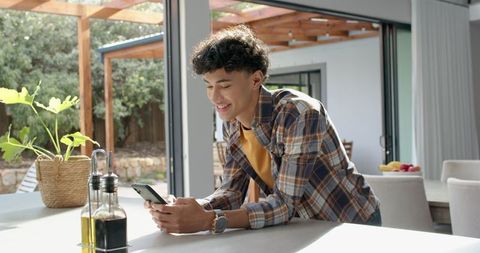 Young Man Using Smartphone in Modern Kitchen with Olive Oil and Vinegar Nearby