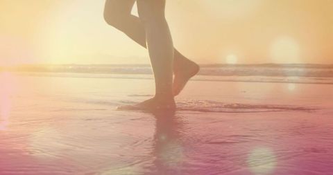 Adult female walking barefoot along wet shoreline at golden hour sunrise with sunlit reflections