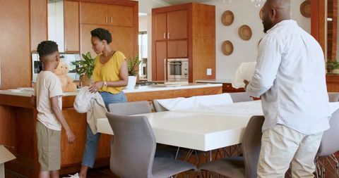 African american family unpacking modern kitchen, folding linens and carrying pillows