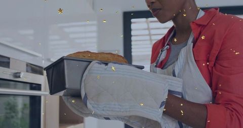 Woman pulling fresh homemade loaf from oven wearing oven mitts and apron