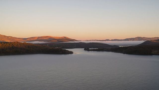 Panoramic Tranquil Sunrise Over Misty Lake and Rolling Hills Reflecting Golden Dawn Light
