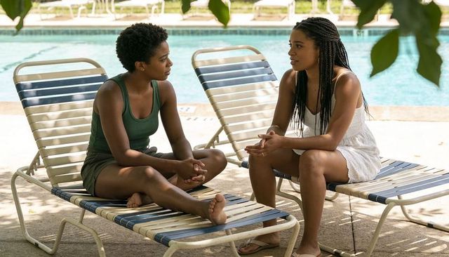 Poolside heart-to-heart: two friends chatting on striped loungers beside turquoise water
