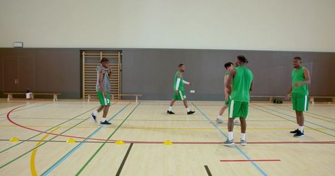 Diverse male basketball team practicing dribbling drills through cones in indoor gymnasium