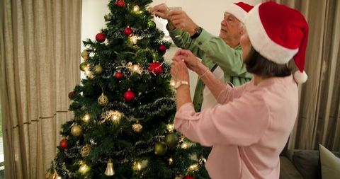 Senior Couple Decorating Christmas Tree at Home with Festive Joy