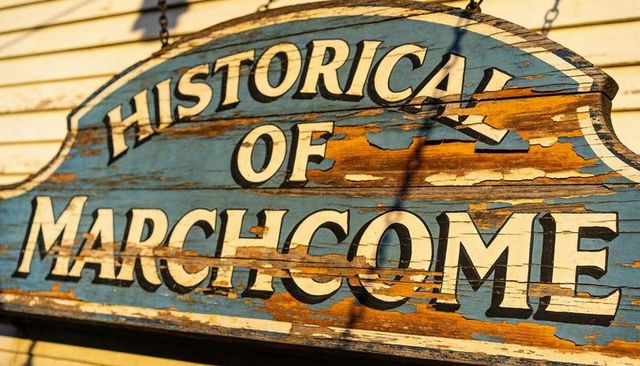 Weathered blue wooden sign showing historical of marchcome with peeling paint and rustic chains