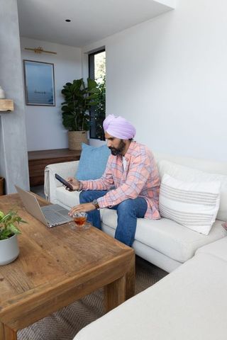 Indian Man with Pink Turban Typing on Laptop in Modern Living Room