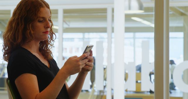 Red-haired woman texting on smartphone inside modern office - Download Free Stock Images Pikwizard.com