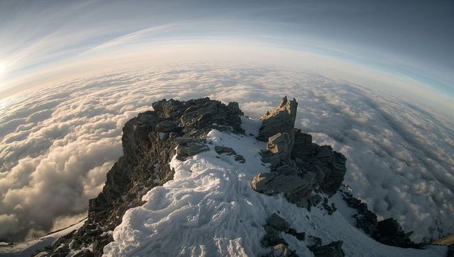 Rising sunlit alpine ridge casting long shadows above sea of clouds at dawn