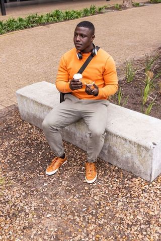 Young african american man sitting on bench enjoying coffee and pastry in urban plaza