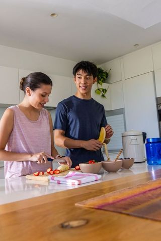 Young couple preparing fresh fruit bowls at bright modern kitchen island for healthy breakfast