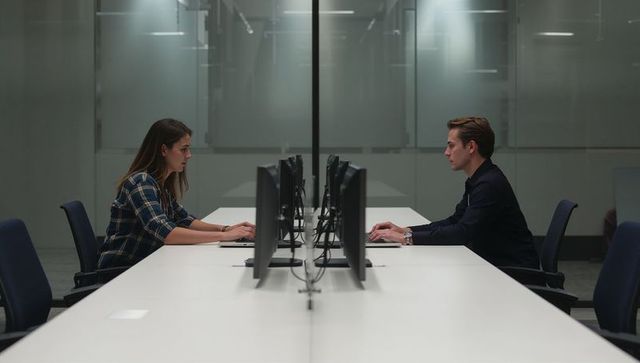 Two professionals working face-to-face at shared desk with dual monitors in modern office