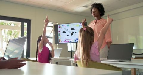 African American teacher guiding students raising hands in modern classroom with laptops