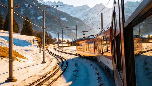 Red electric train curving through snowy alpine valley reflecting golden light
