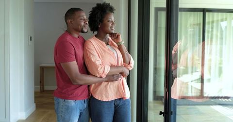 African american couple embracing by sliding glass door in modern home with natural light