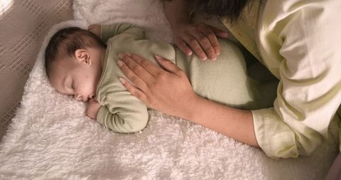 Tenderly mother watching over her sleeping baby in cozy nursery setting