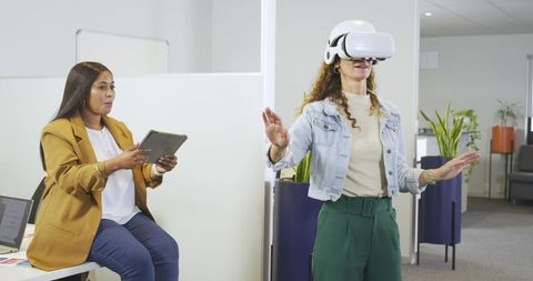 Diverse female coworkers testing vr headset while colleague recording on tablet in office