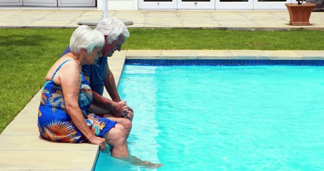 An elderly couple is sitting at the edge of a swimming pool, dipping their feet in the water on a sunny day. Ideal for use in advertisements promoting senior lifestyle, retirement communities, health and wellness for seniors, vacation spots, or leisure activities.