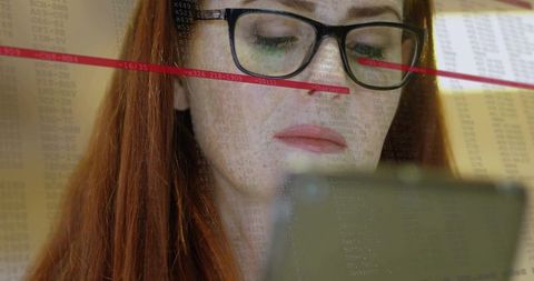 Red-haired woman analyzing data on smartphone wearing black glasses, closeup showing focus in office