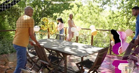 Friends decorating sunlit backyard deck for 30th birthday with gold number 30 balloon