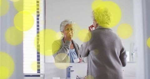 Senior woman applying lip balm at bathroom mirror morning self-care routine