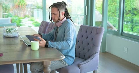 Mid-adult african american man working remotely at sunlit glass-walled dining table
