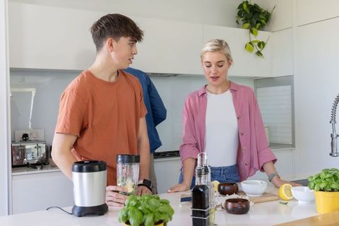 Teenager preparing smoothie with parent in bright modern kitchen, cooking together