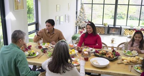 Extended family sharing festive meal at wooden table with roast chicken and fireplace