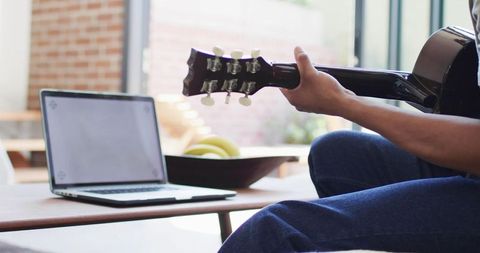 Man uses laptop for guitar practice at home
