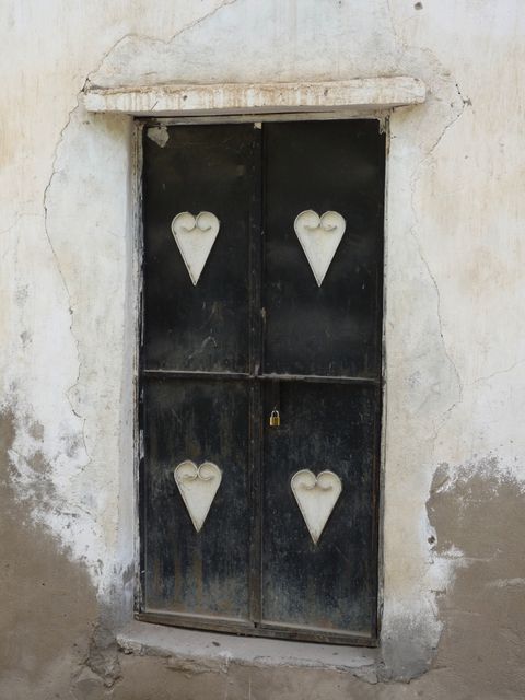 Old-fashioned, rustic door features heart-shaped cutouts on panels, ideal for illustrating themes of romance and history. Weathered walls and traditional design make perfect material for projects on vintage architecture or pastoral life. Use in home decor inspiration, historical restoration showcases, or romantic designs.