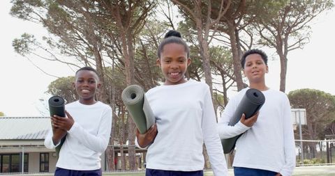 Children carrying exercise mats outdoors on sunny day