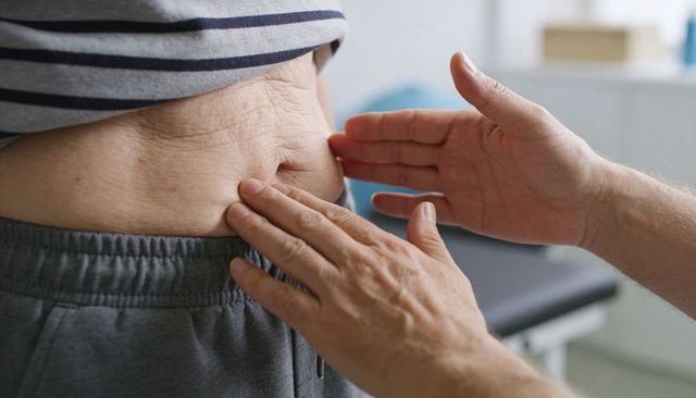 Clinician palpating patient abdomen and navel during routine physical examination
