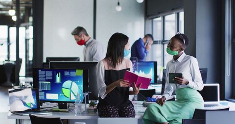 Diverse Female Colleagues in Masks Discussing Work in Modern Office