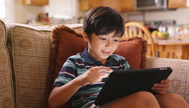 Smiling Boy Using Tablet on Cozy Couch in Kitchen Living Room for Family Tech Education