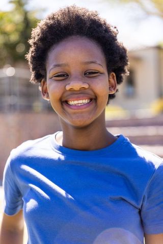 African american teen smiling wearing bright blue t-shirt sunlit outdoor portrait with bokeh