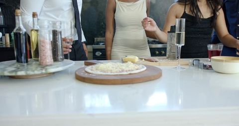 Dressy african american friends making pizza at modern kitchen island with champagne