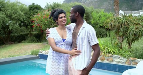 Indian woman and african american man embracing at poolside in sunny suburban garden